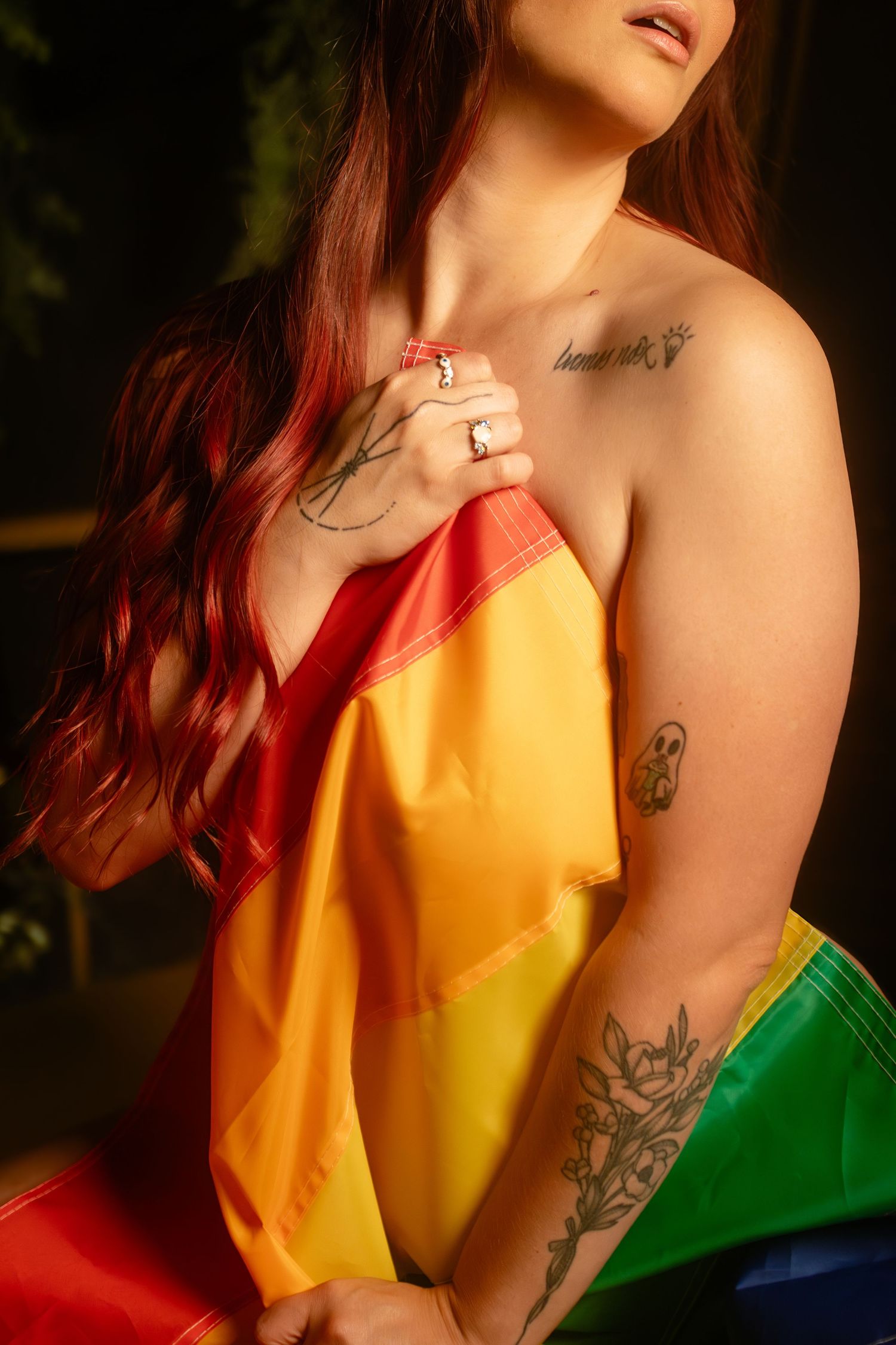 Close-up of person draped in rainbow flag showing tattoos in inclusive Fort Worth boudoir session for Pride Month.