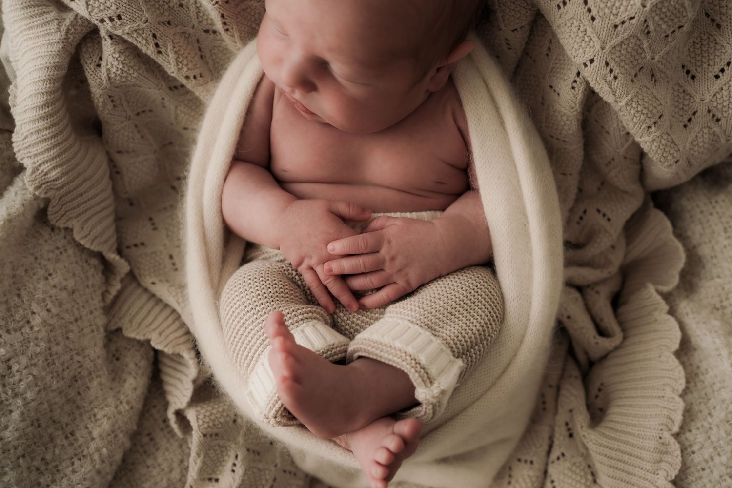 Newborn baby wrapped in cream colored blanket lying on textured beige backdrop in calm sleeping pose in Healesville, Victoria
