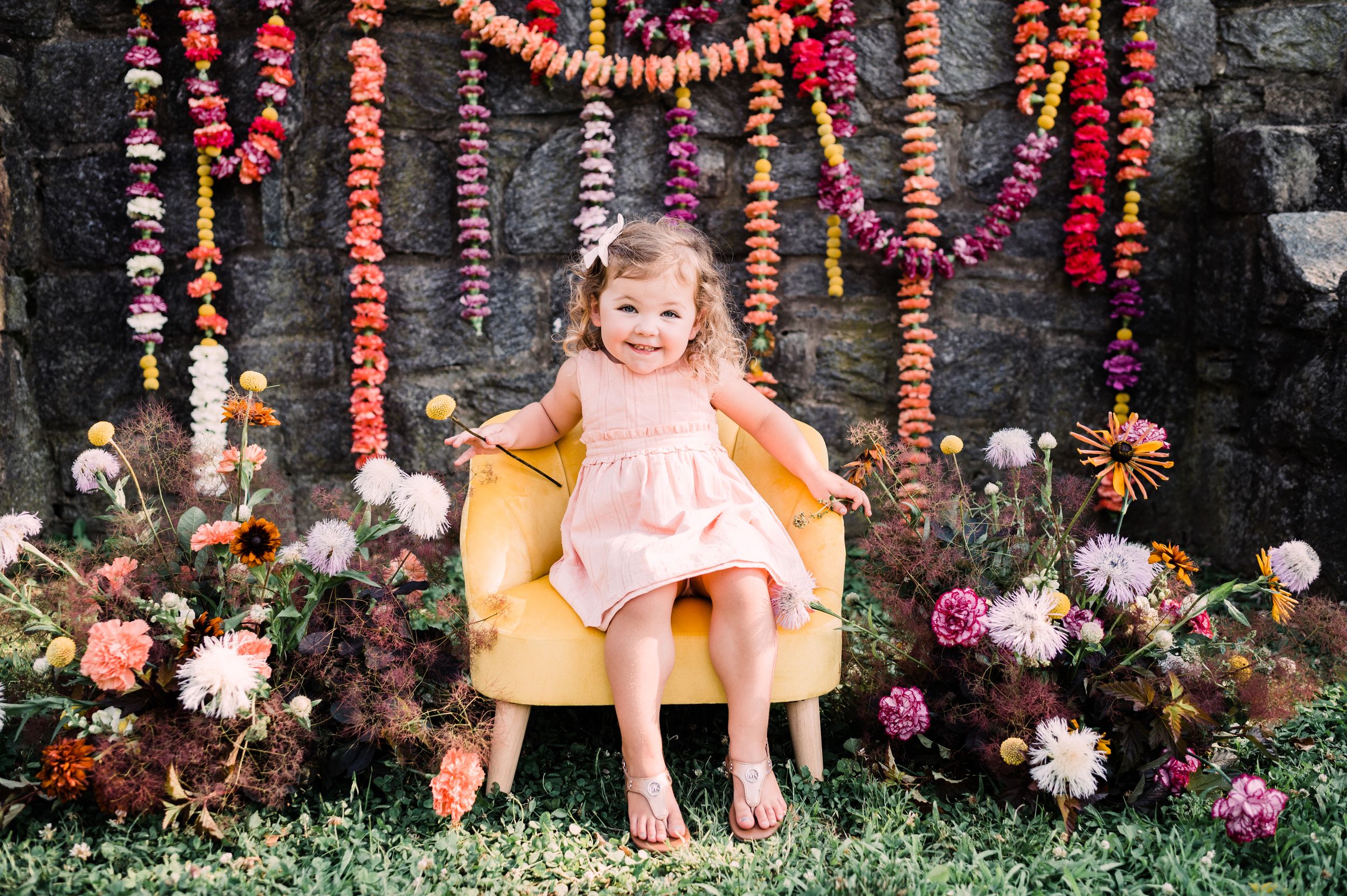 A yellow chair adorned with floral decorations and hanging strings of colorful beads creates a whimsical garden backdrop.