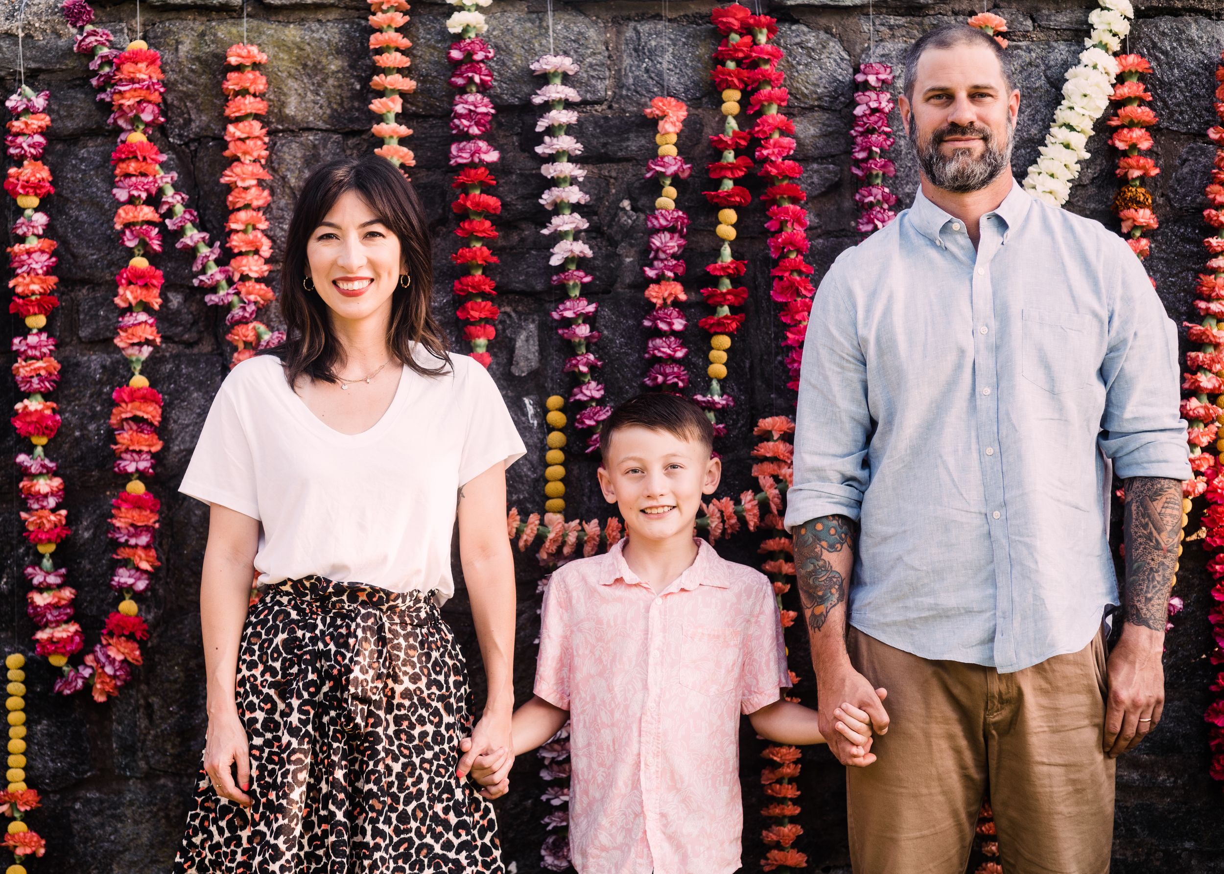 Family photo session against stone wall decorated with vibrant red and pink hanging flower strands.