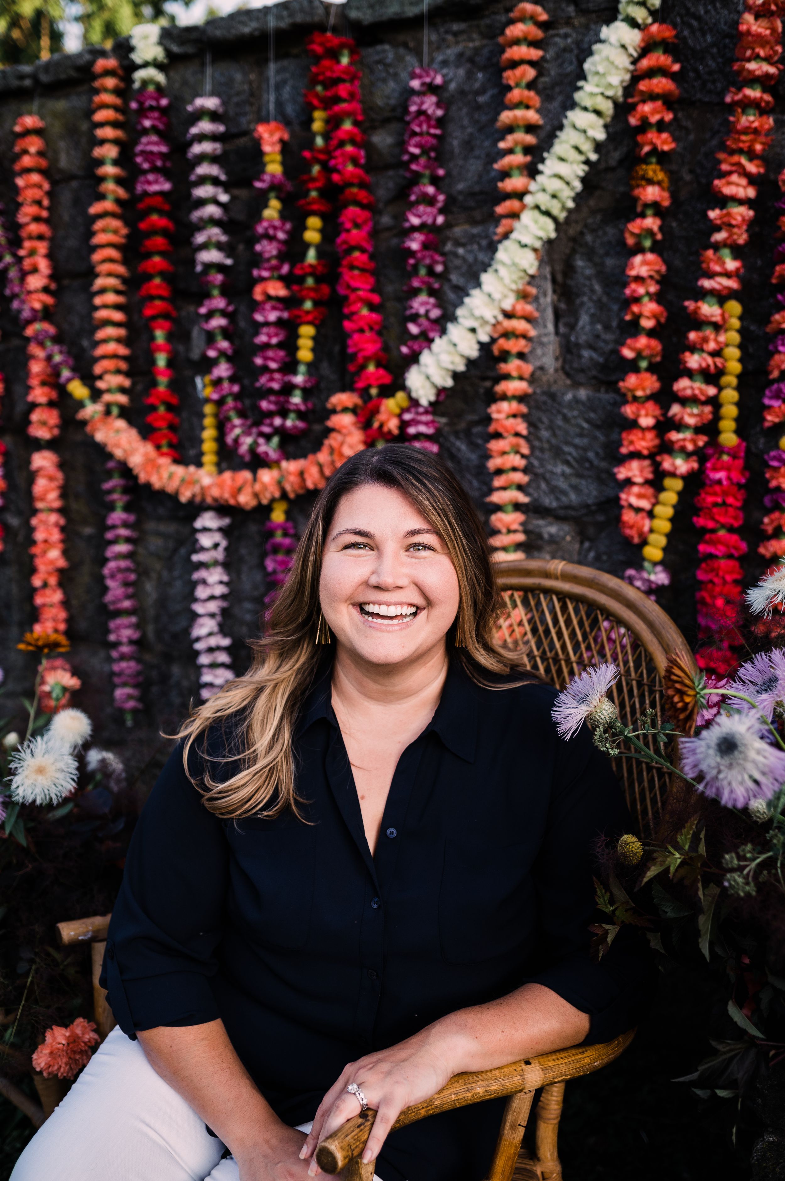 Outdoor portrait against stone wall with hanging pink and orange flower garlands and decorative backdrop.