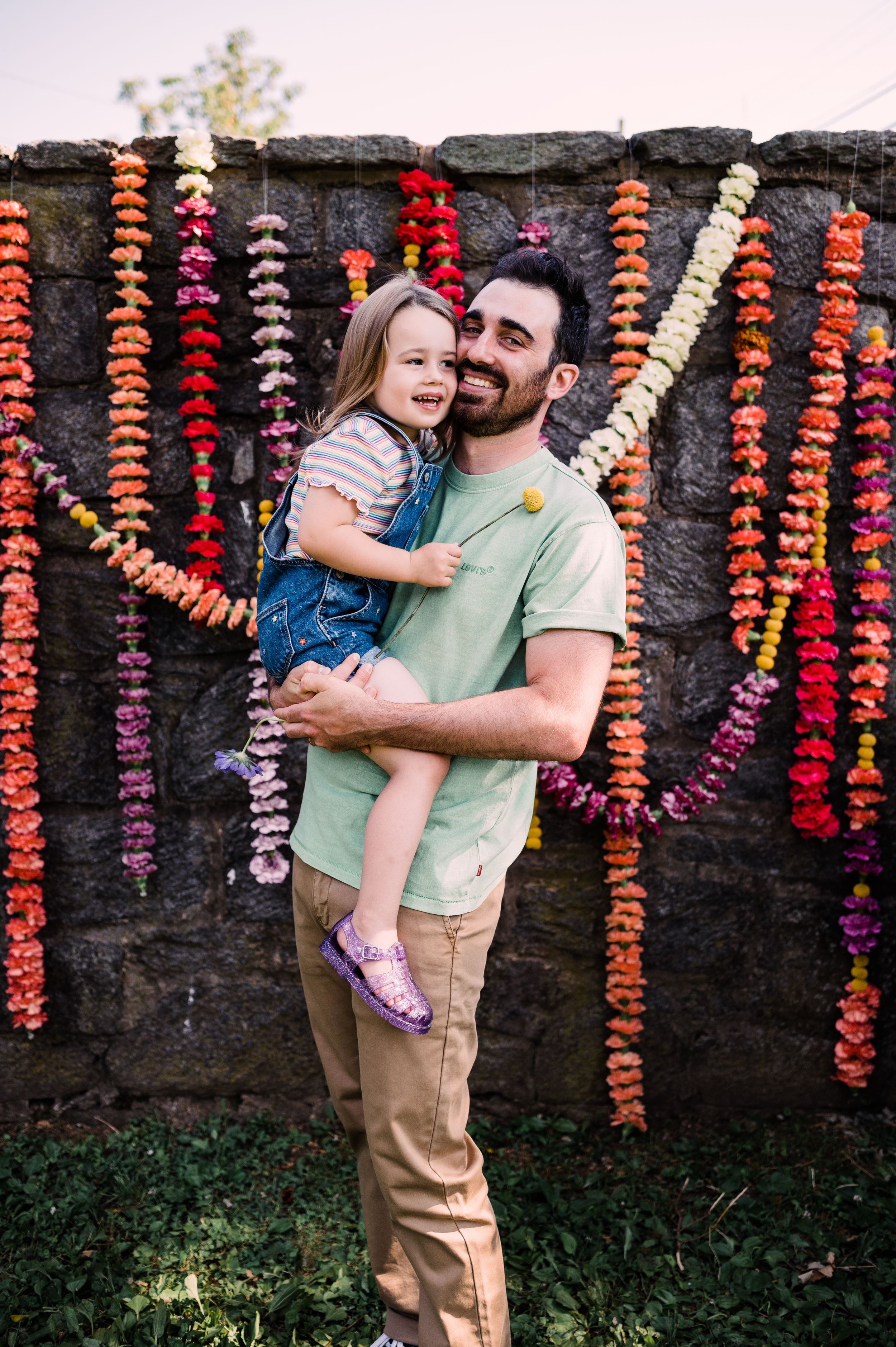 Stone wall backdrop decorated with cascading pink and red flower garlands for outdoor portrait session.