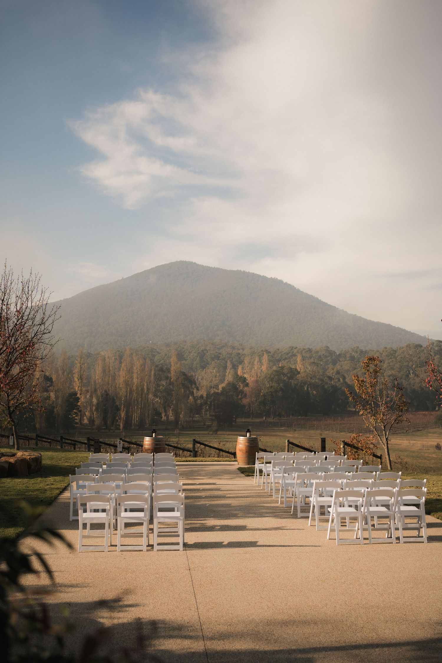 Outdoor wedding ceremony setup with white chairs facing mountain backdrop.