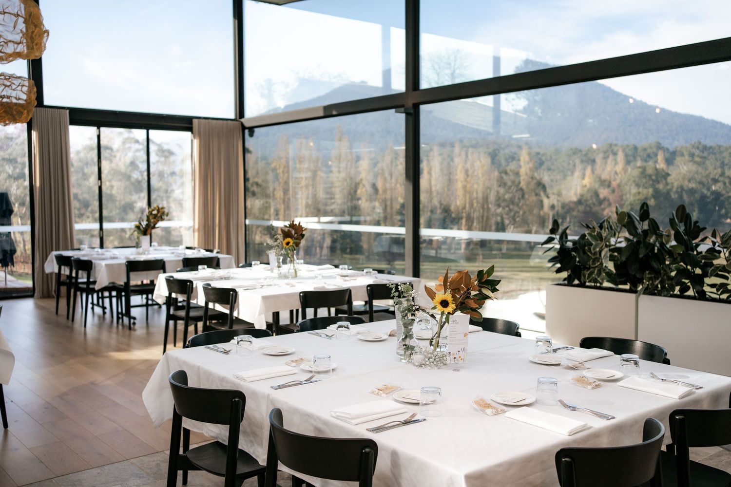Modern restaurant interior with panoramic mountain views, white tablecloths, and elegant table settings.