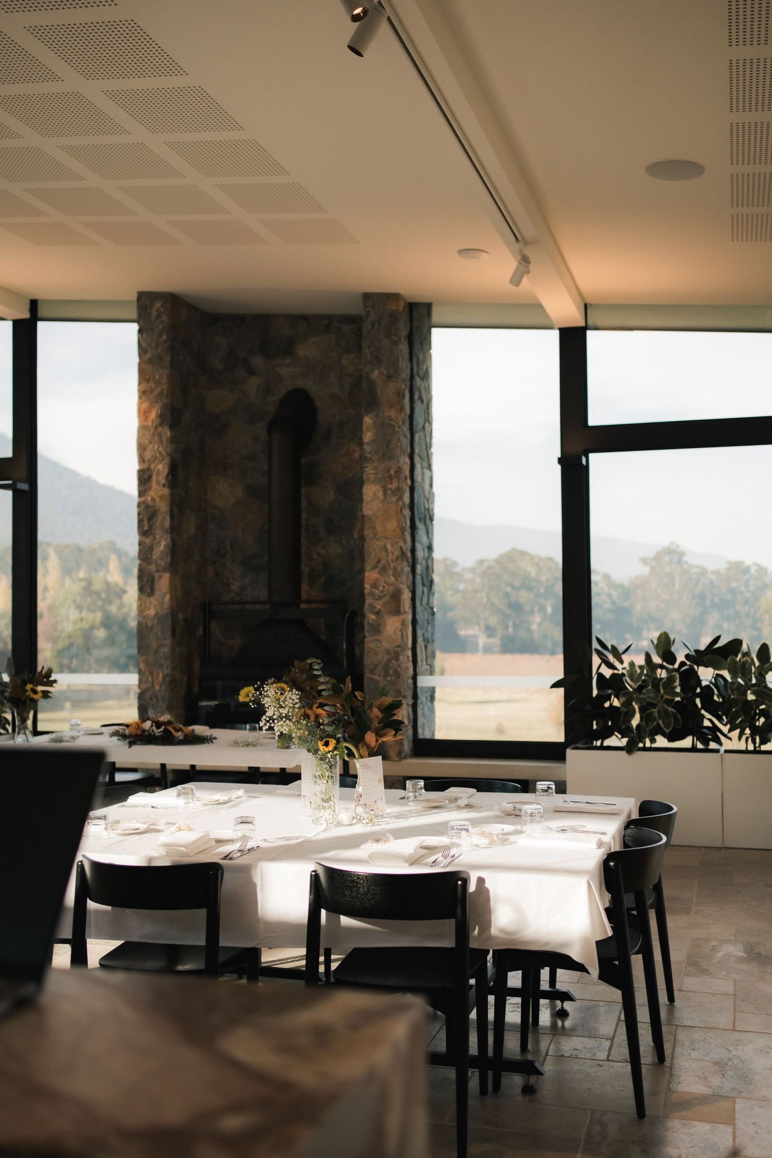Modern dining room with stone fireplace, white tablecloths, and panoramic mountain views through large windows.