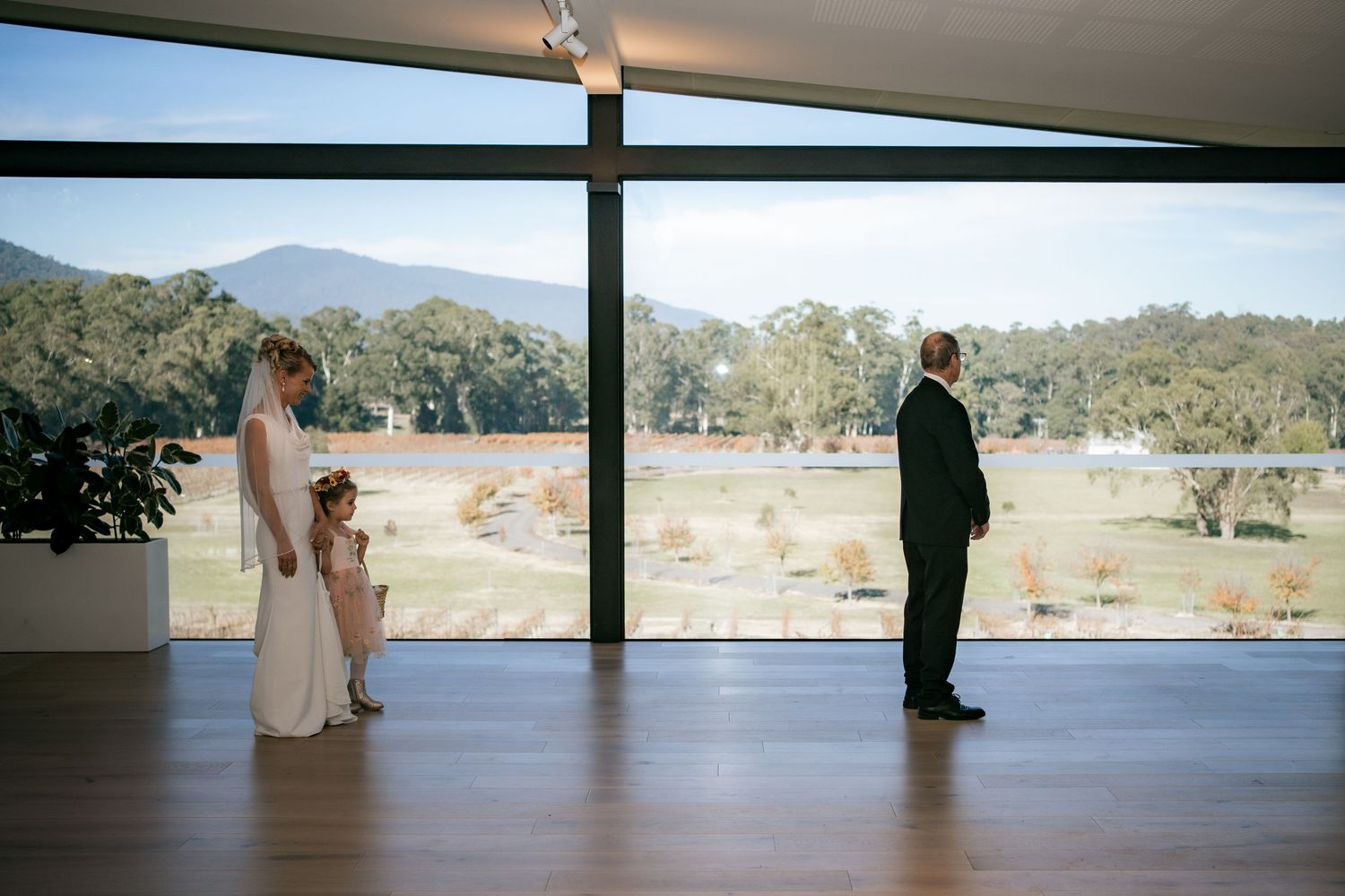 Wedding ceremony silhouettes against floor-to-ceiling windows overlooking a scenic lake and mountains.