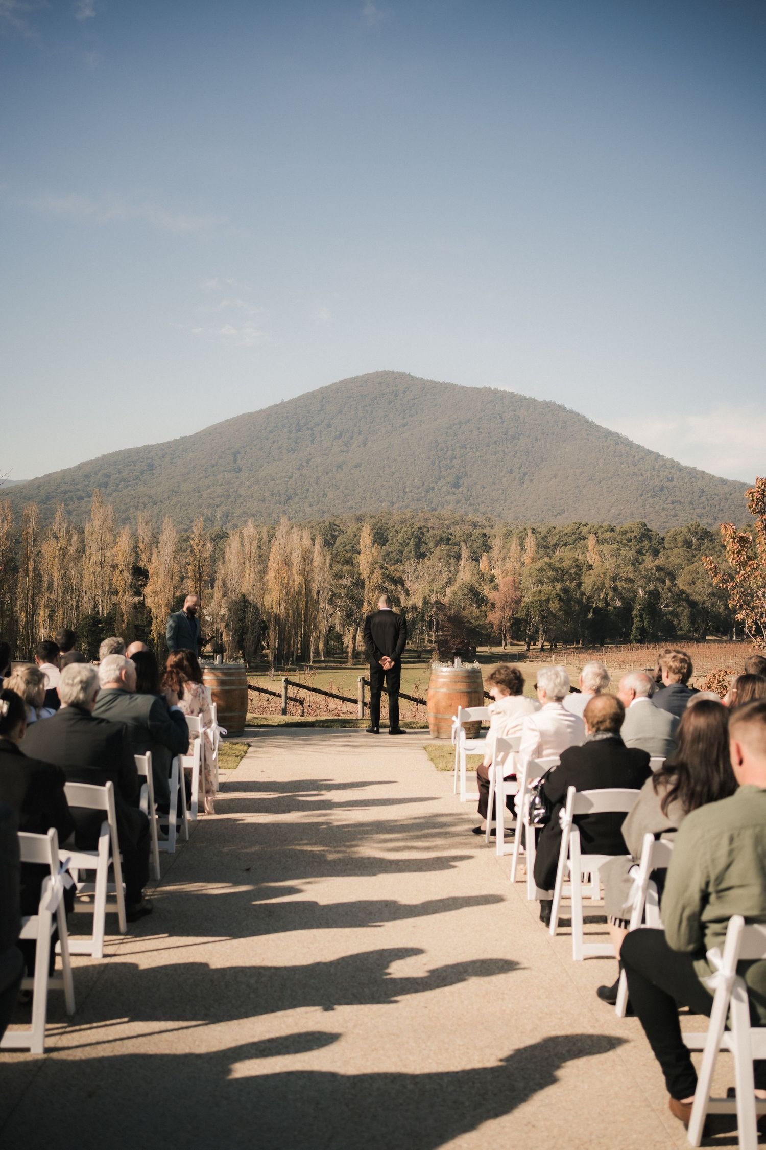 Outdoor wedding ceremony setup with white chairs facing a mountain backdrop at sunset.
