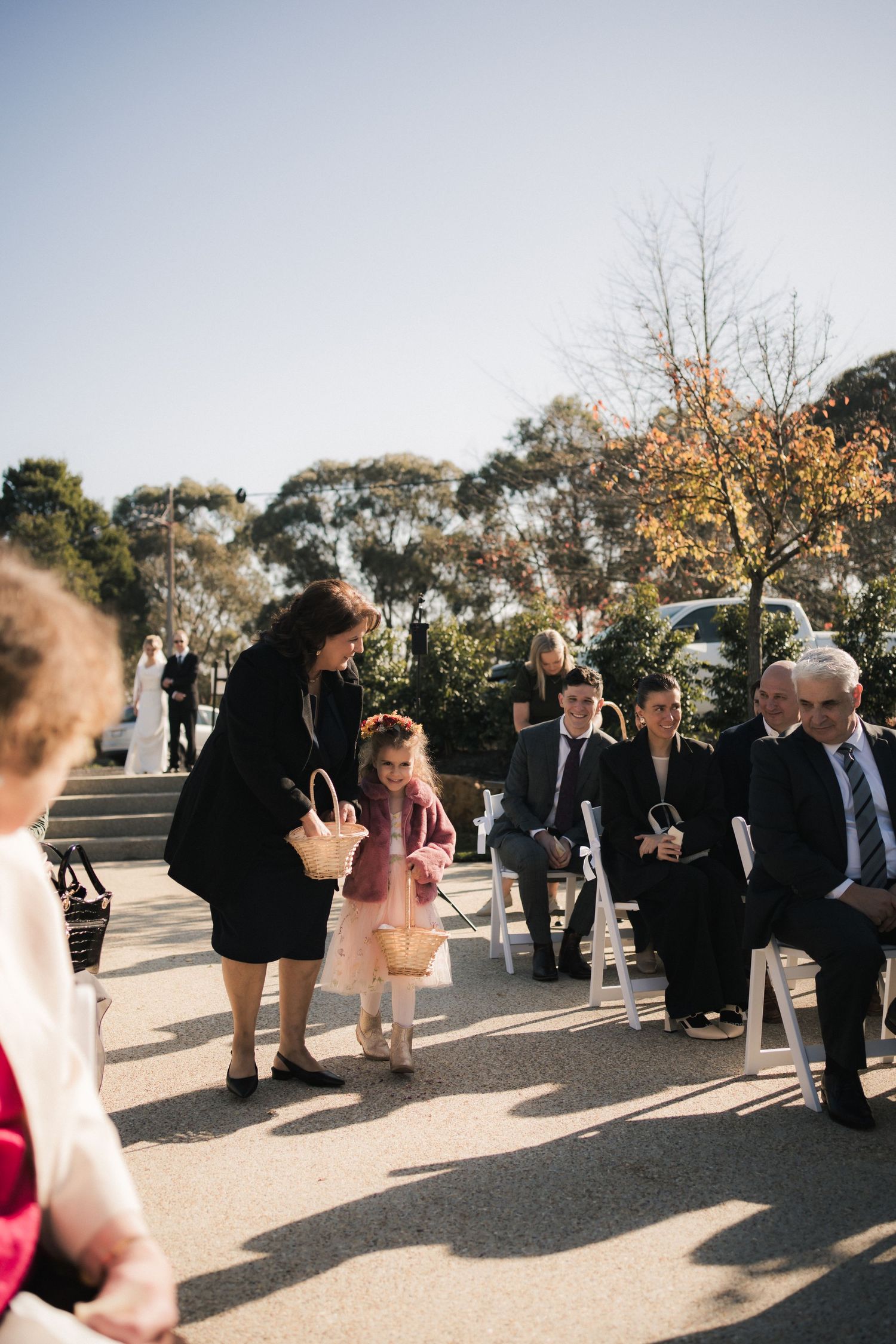 Wedding guests mingling and socializing on a paved outdoor venue area surrounded by trees.