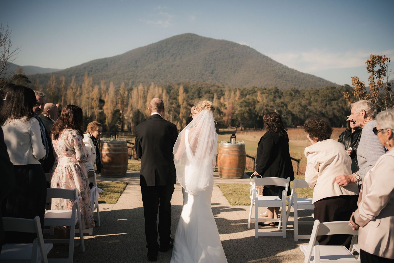 An outdoor wedding ceremony takes place against a backdrop of mountains and autumn trees at a vineyard venue.