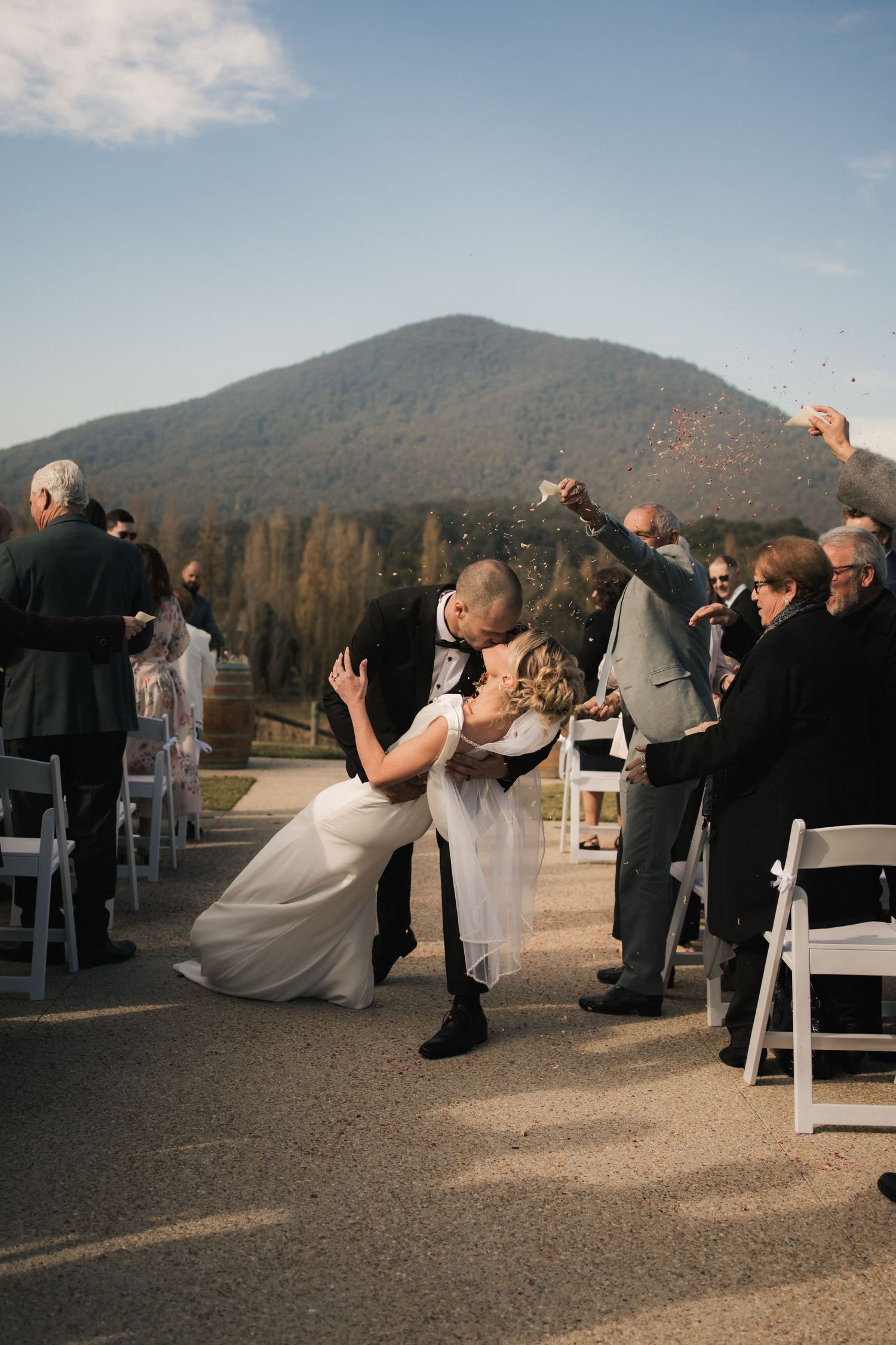 A romantic outdoor wedding ceremony with a mountain backdrop as guests throw confetti during the celebration.