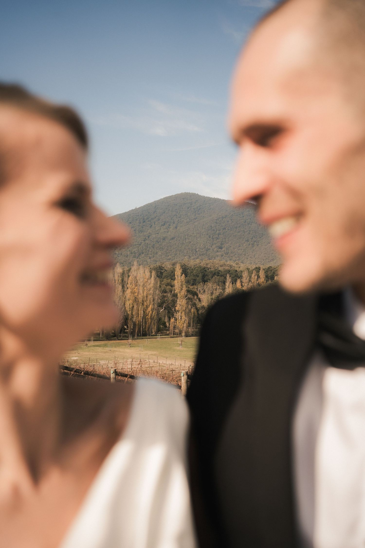 Close-up shot of a couple with scenic mountain cliffs and lake in the background.