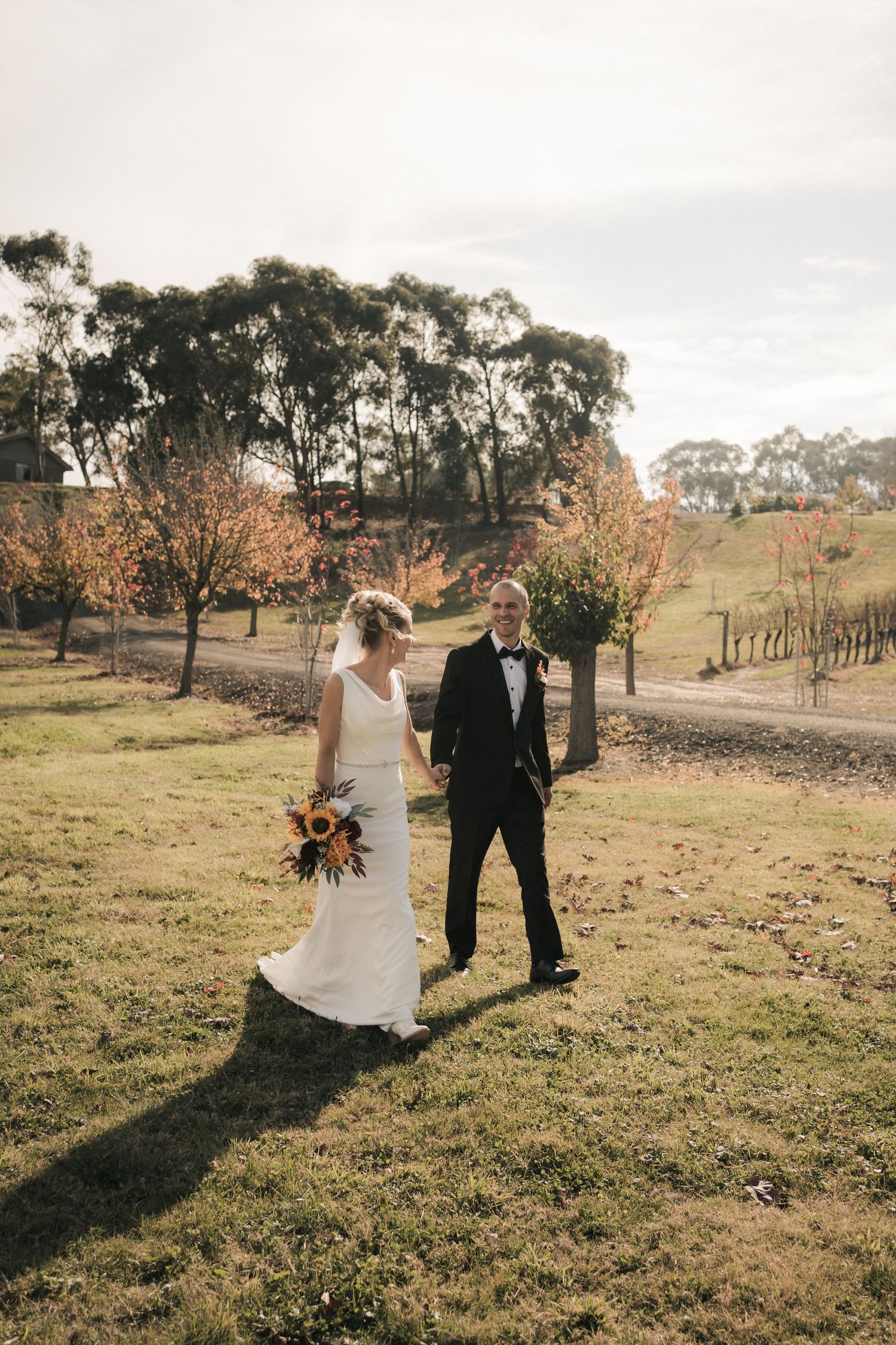 Wedding couple walking together through a scenic vineyard with autumn foliage and rolling hills.