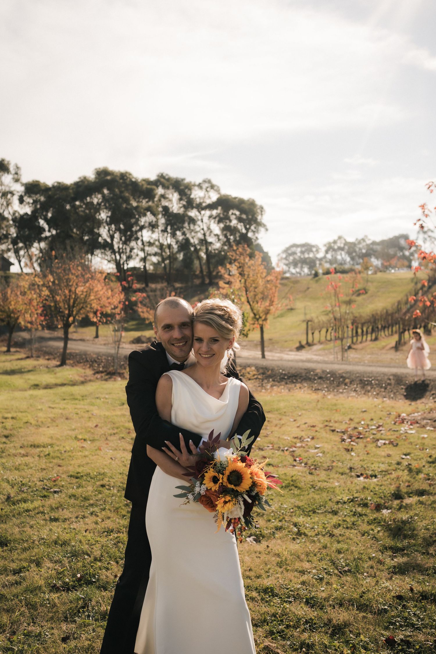 Couple embraces in rustic outdoor vineyard setting with autumn foliage.
