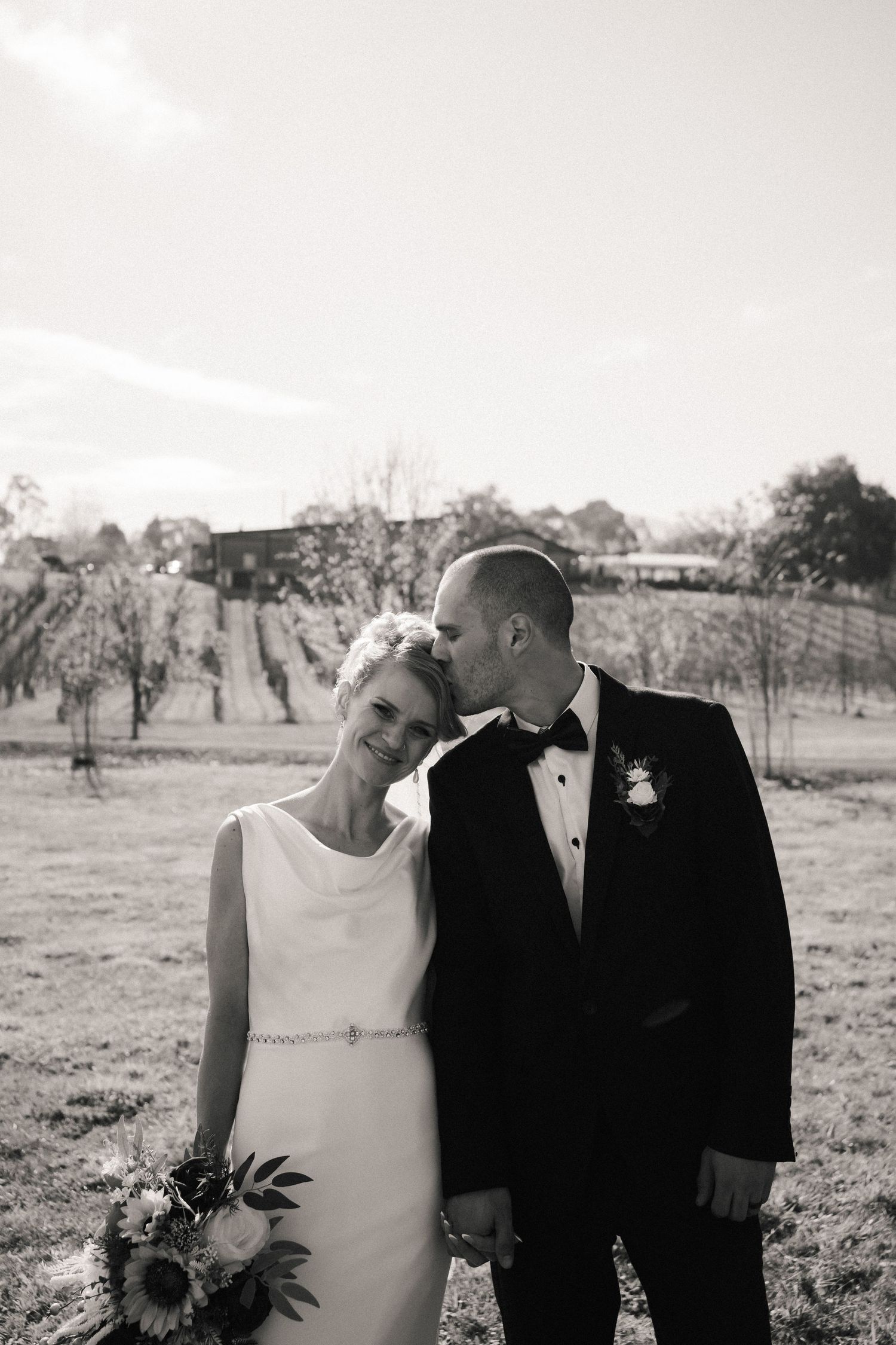 A romantic wedding portrait of newlyweds in a vineyard setting captured in black and white.