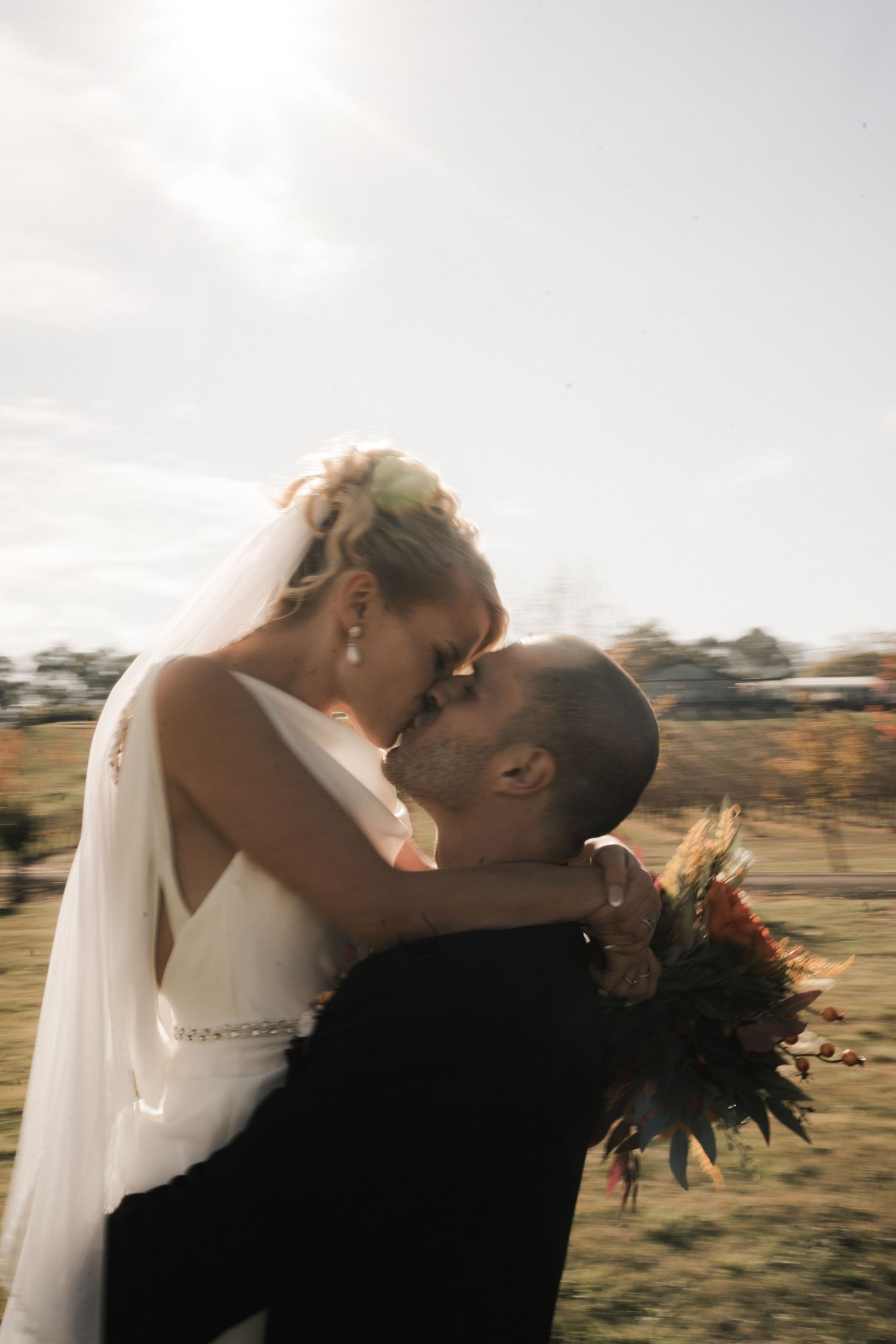 A wedding couple shares an intimate moment against a rustic countryside landscape during golden hour.
