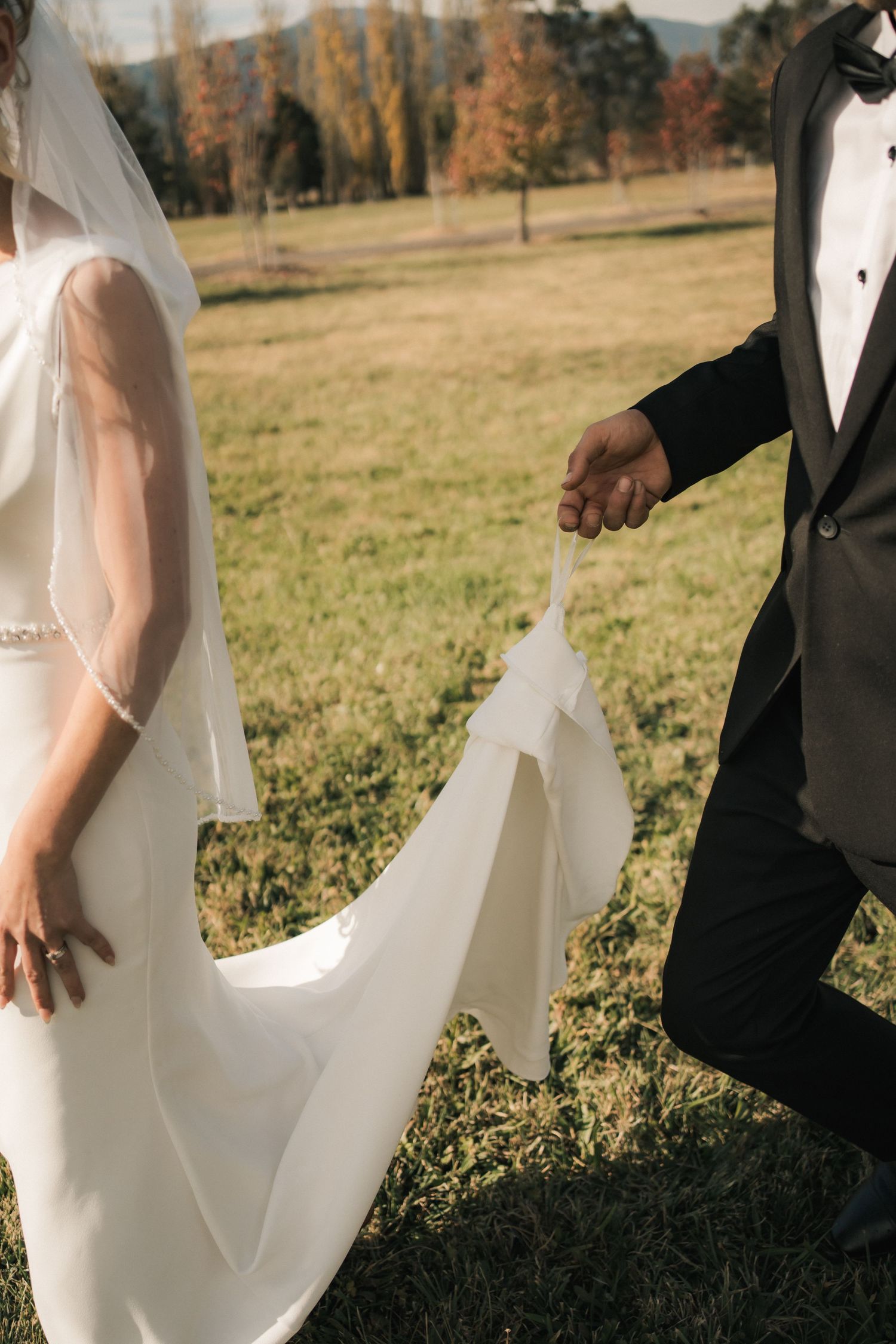 Detail shot of bride's white wedding dress train held in grassy outdoor setting.