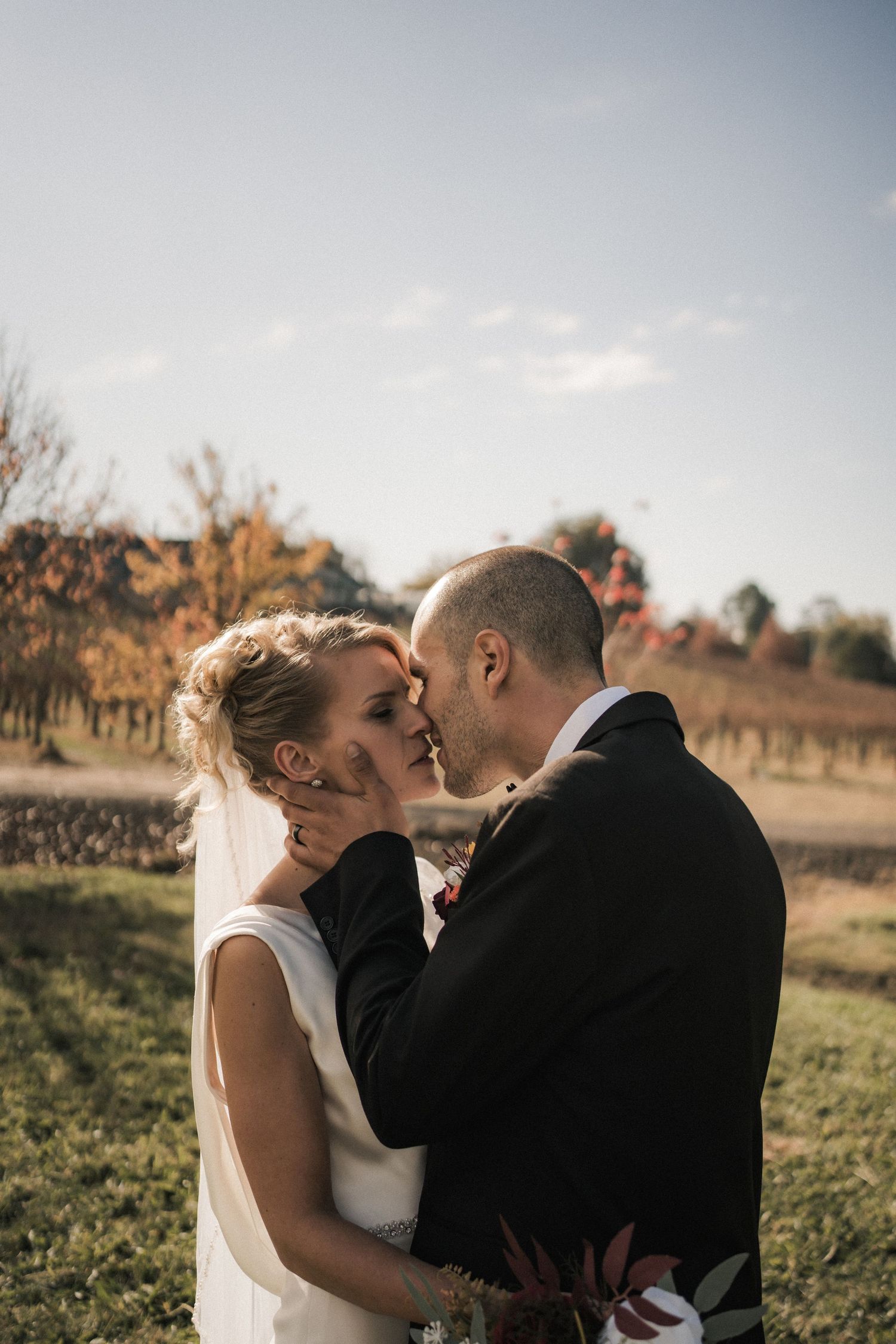 Intimate wedding couple moment in golden light among vineyard rows.