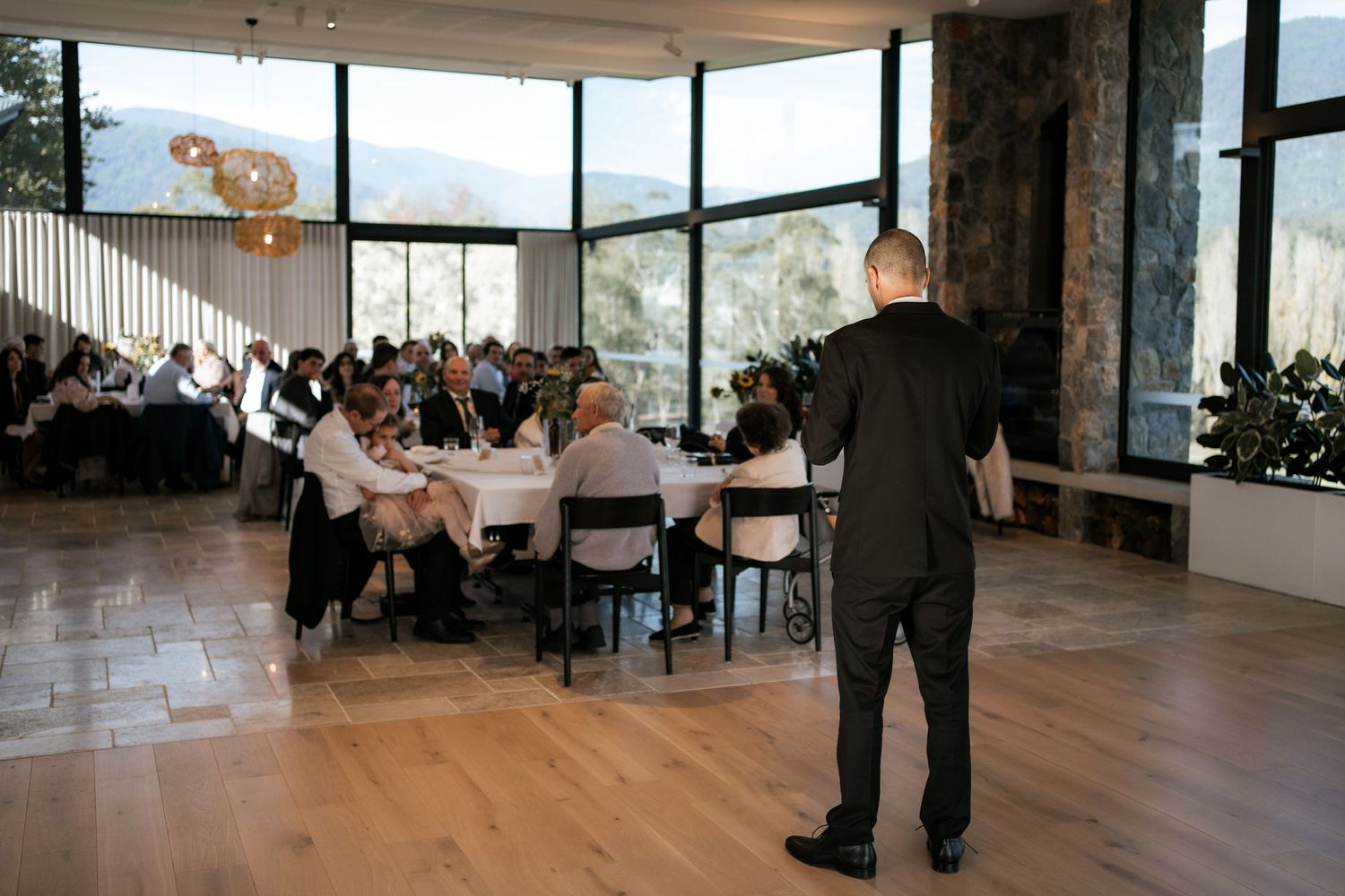 Wedding reception venue with guests seated at tables while speaker addresses crowd.