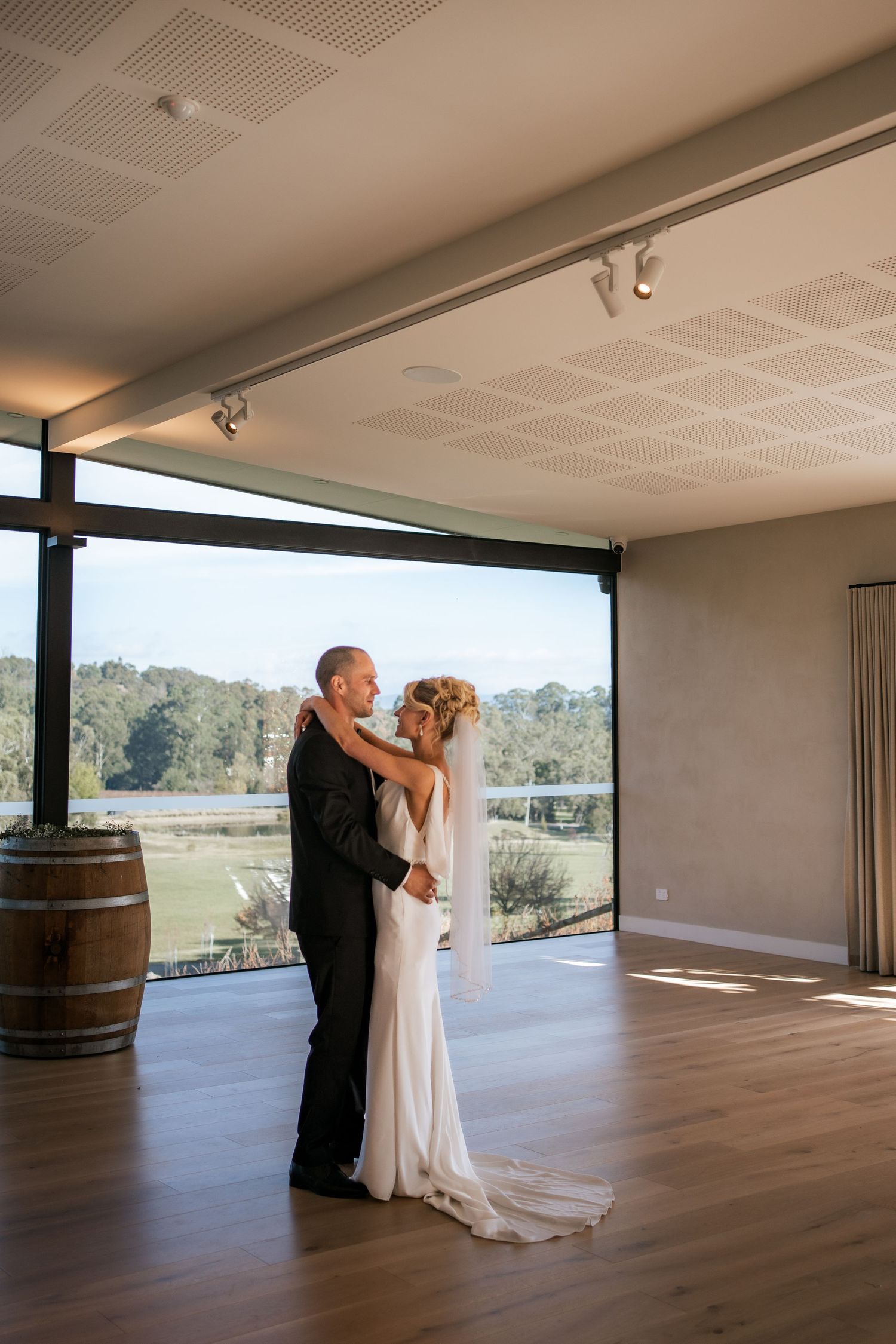 Bride and groom share an intimate dance in a modern venue with wooden floors and barrel decor.