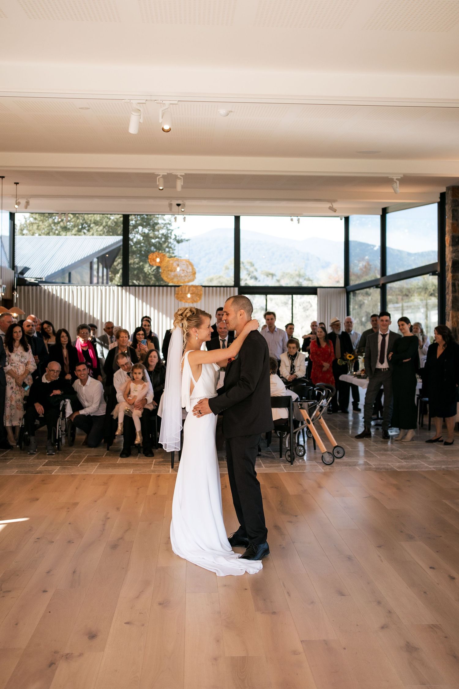 Couple shares their first dance in a modern venue with mountain views and gathered guests.