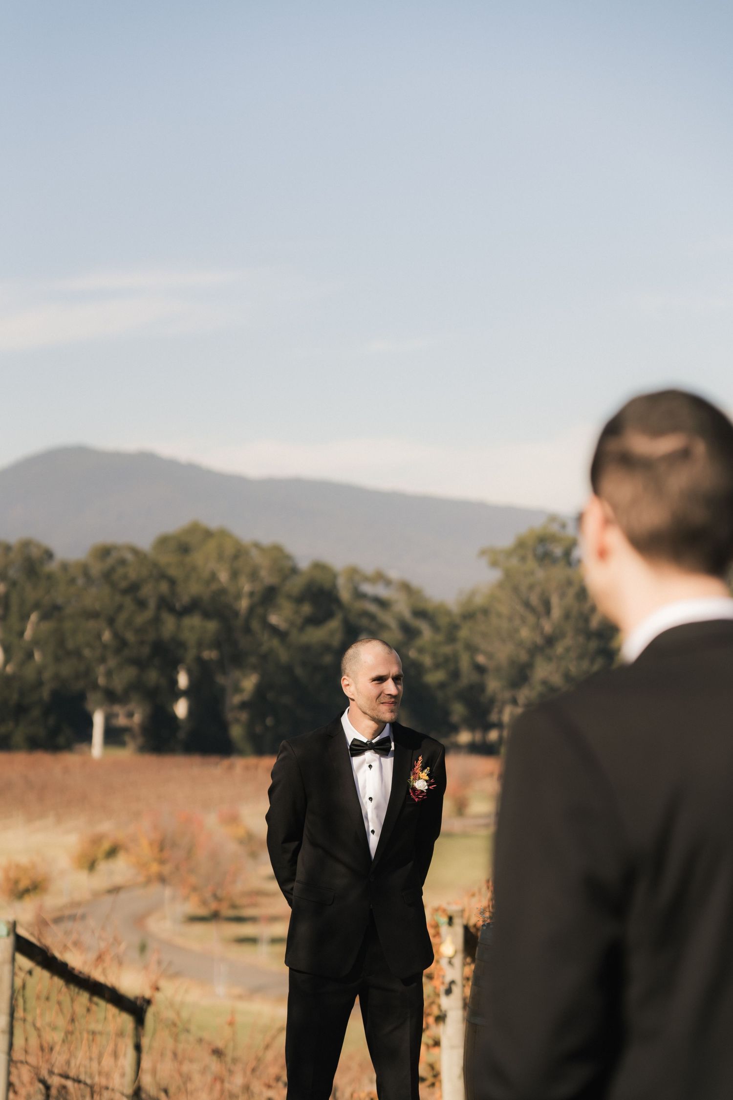 Wedding party in formal attire laughs together in outdoor field at sunset.