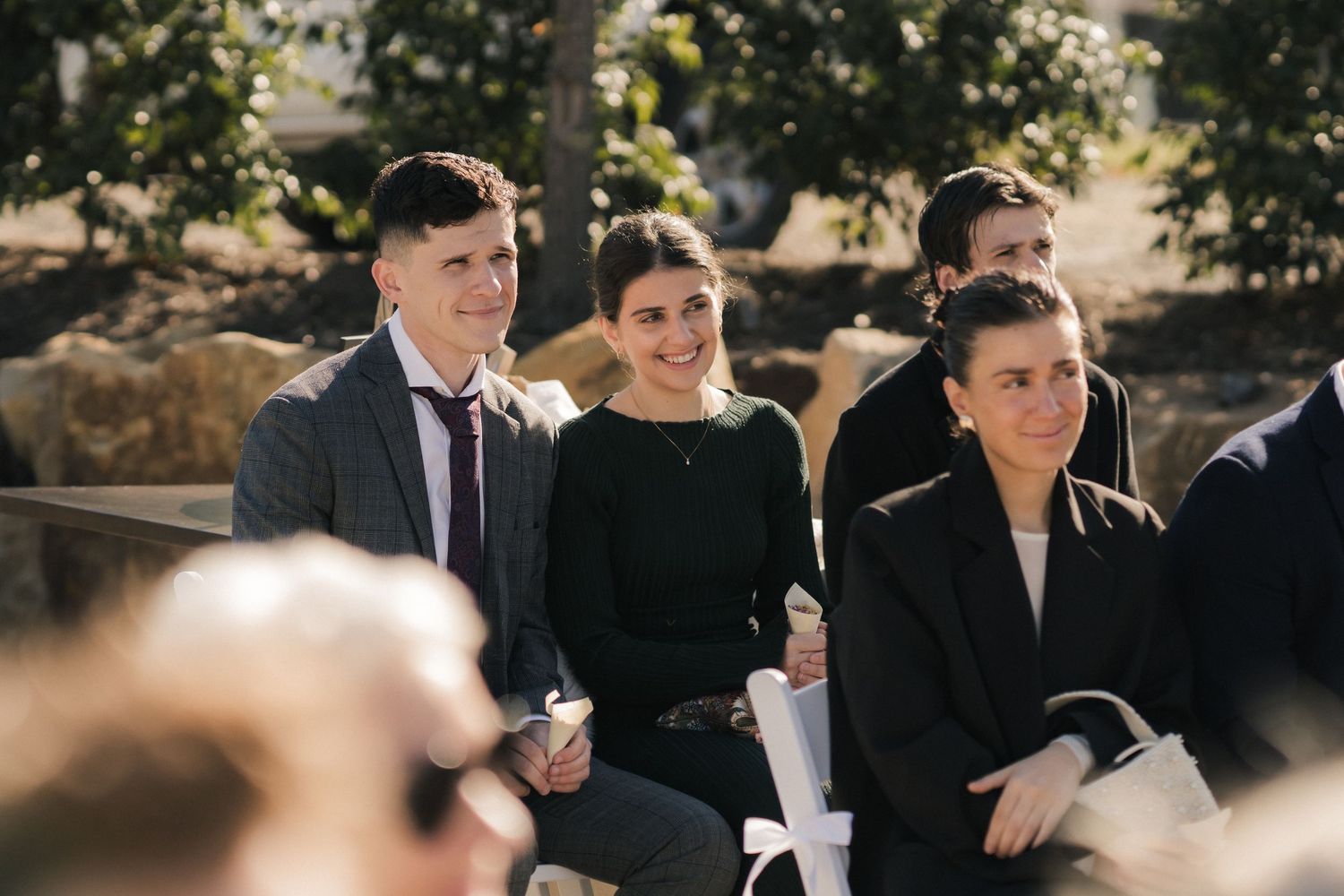 Elegantly dressed people in black and white formal attire gather outdoors during a daytime event.