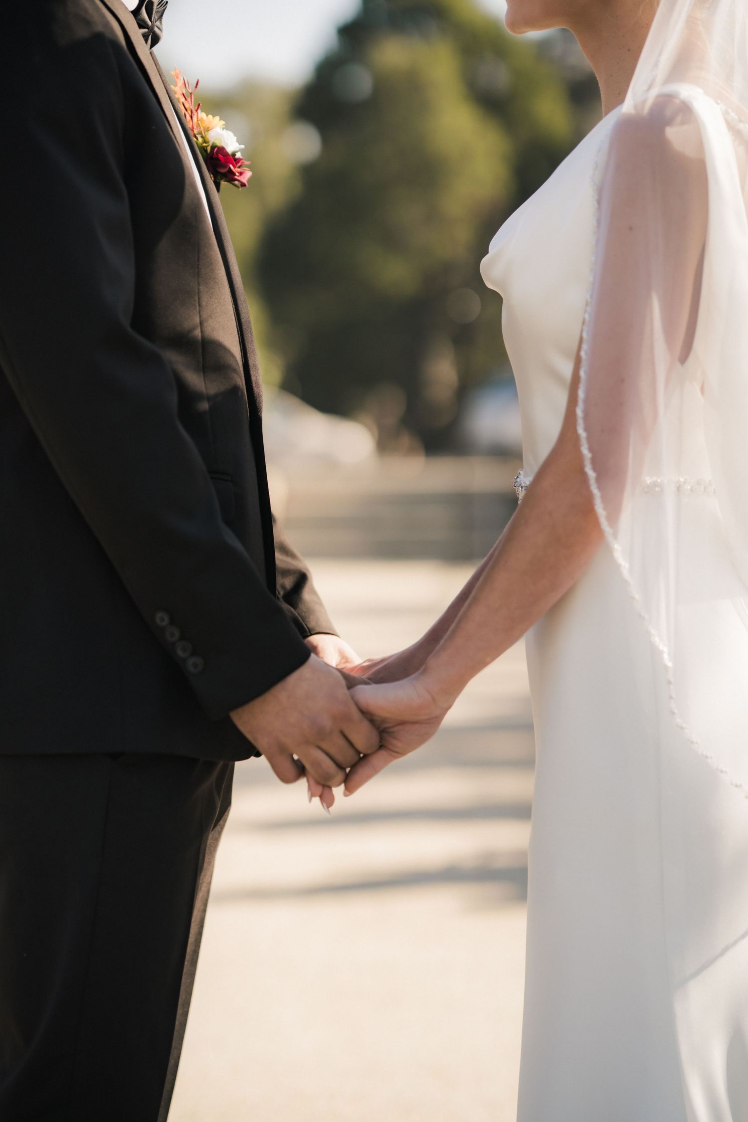 Close-up view of a bride and groom holding hands during their outdoor wedding ceremony.
