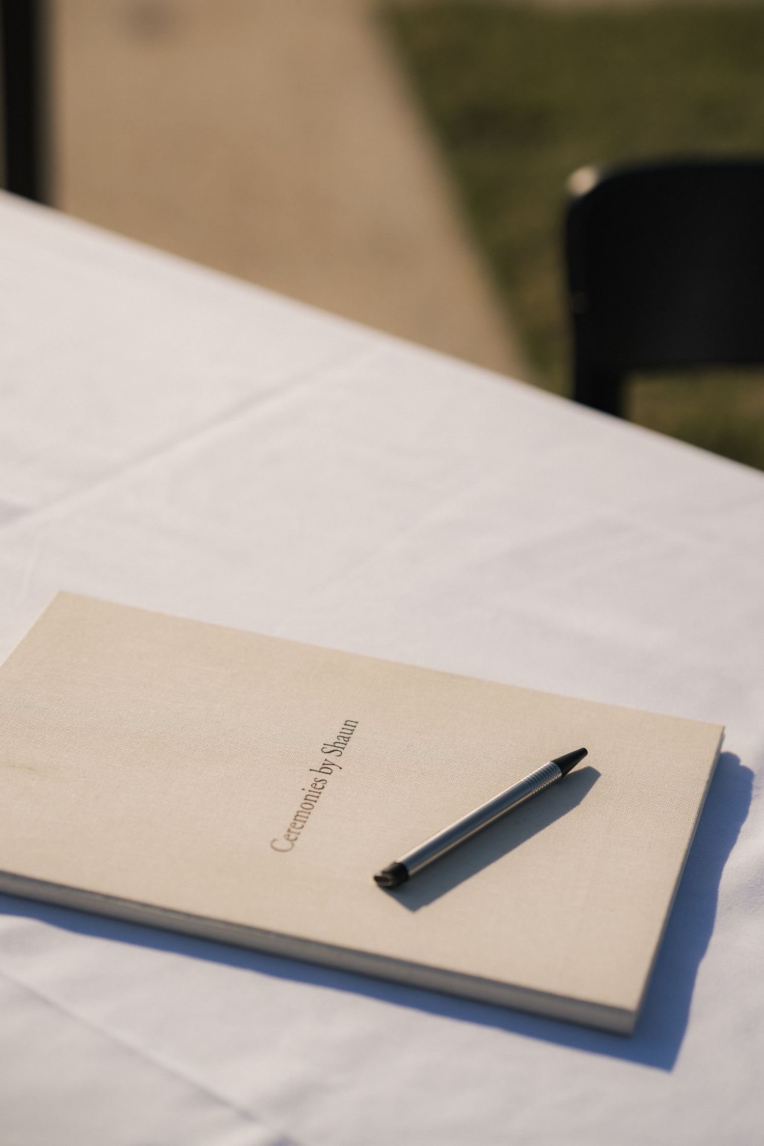 A minimalist notebook and pen rest on a white table surface in soft natural lighting.