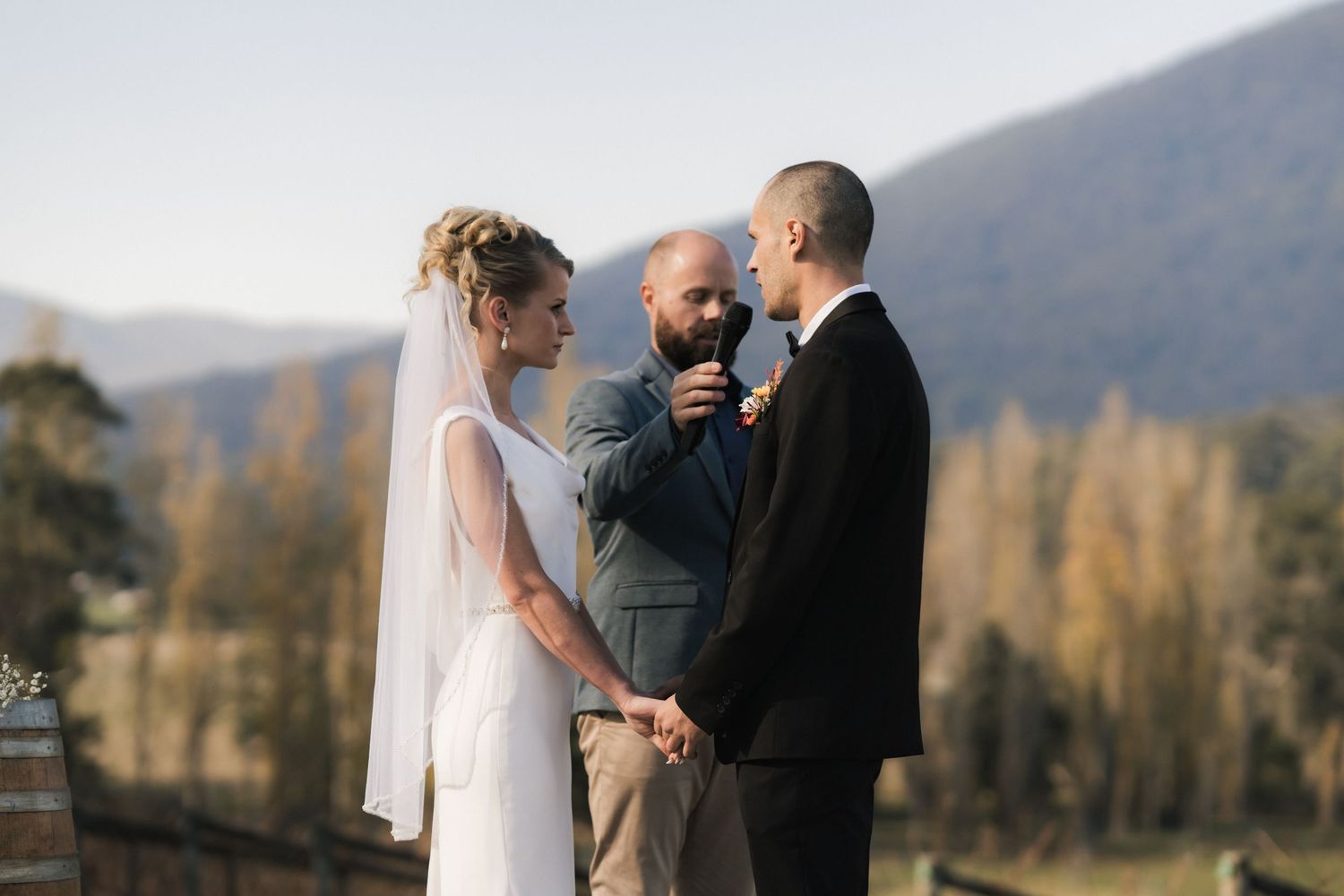 A romantic outdoor wedding ceremony takes place with a backdrop of mountains and autumn trees as a couple exchanges vows.