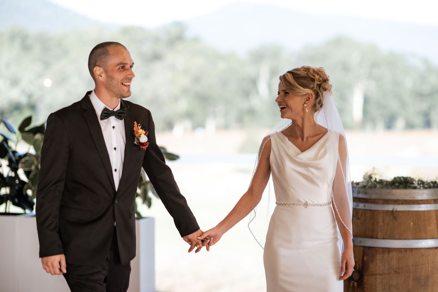 Joyful couple shares candid moment during wedding reception by wine barrel.