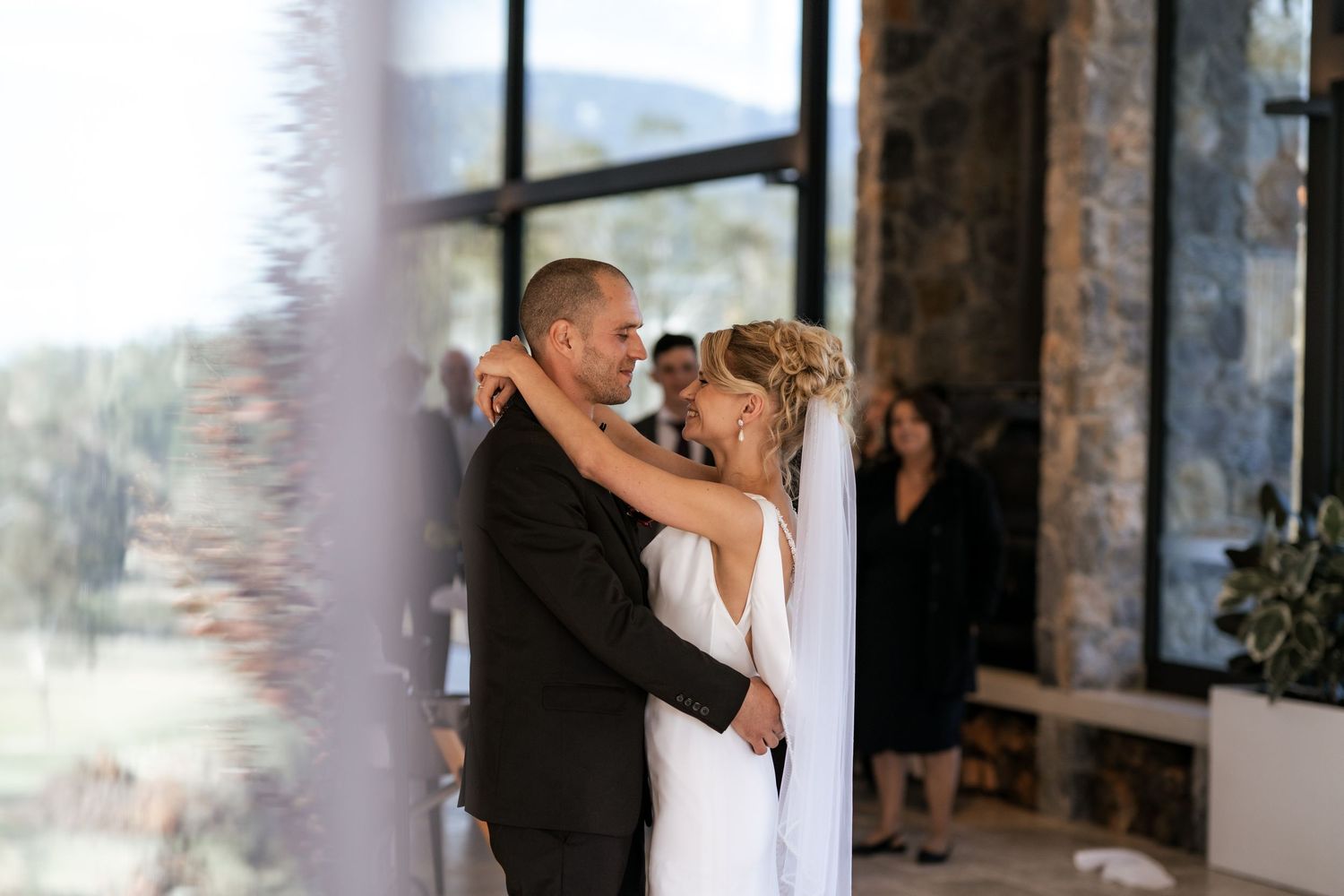 Wedding couple sharing an intimate moment in front of large windows at stone venue.
