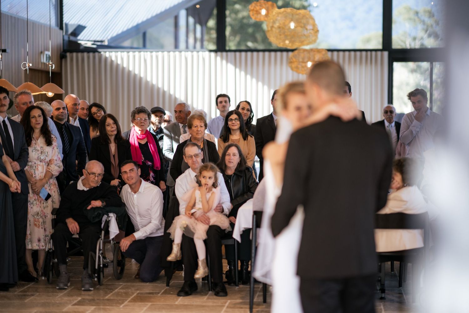 Wedding guests gathered to watch speeches during an indoor reception ceremony.