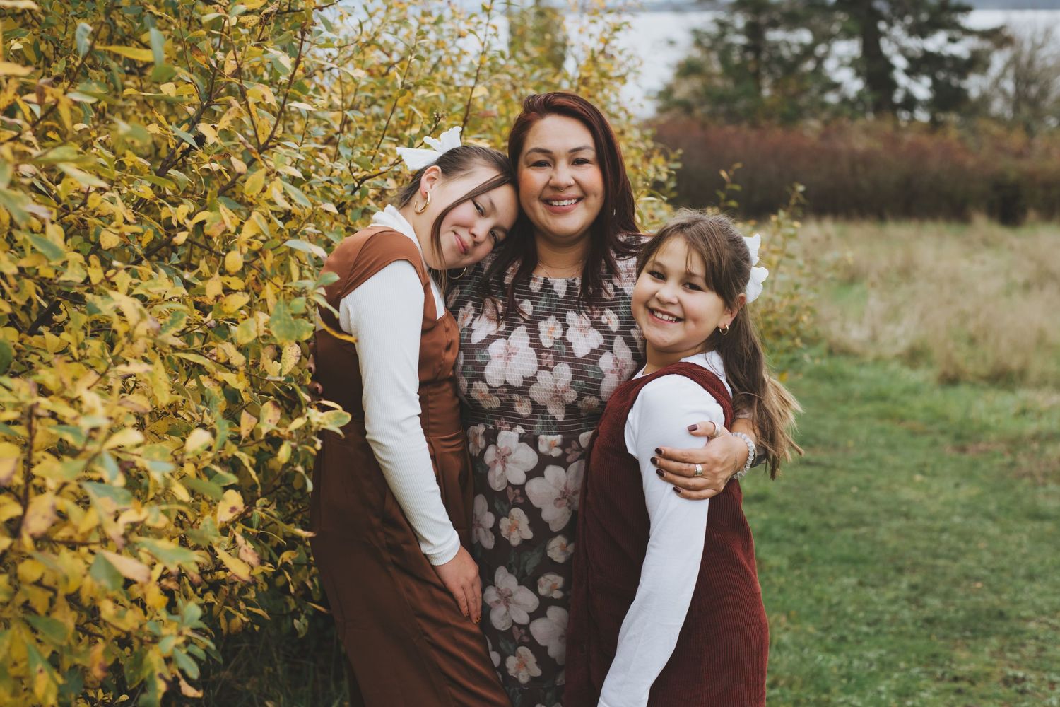 Mother embracing her two daughters with love, surrounded by vibrant autumn foliage.
