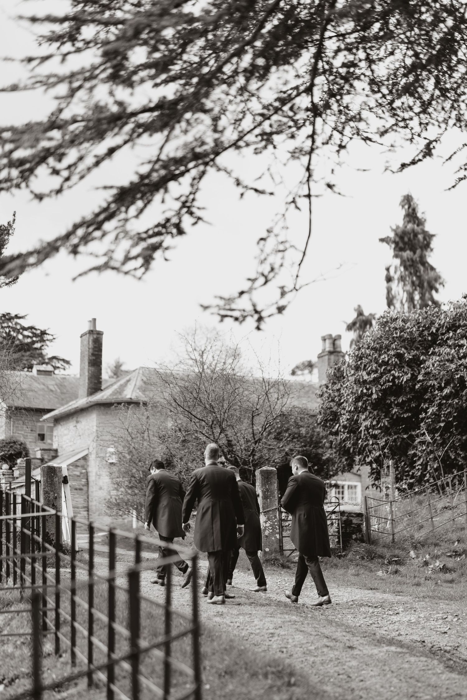 Vintage black and white photo showing people walking on a path beside old buildings and tree branches overhead at Walcott Hall