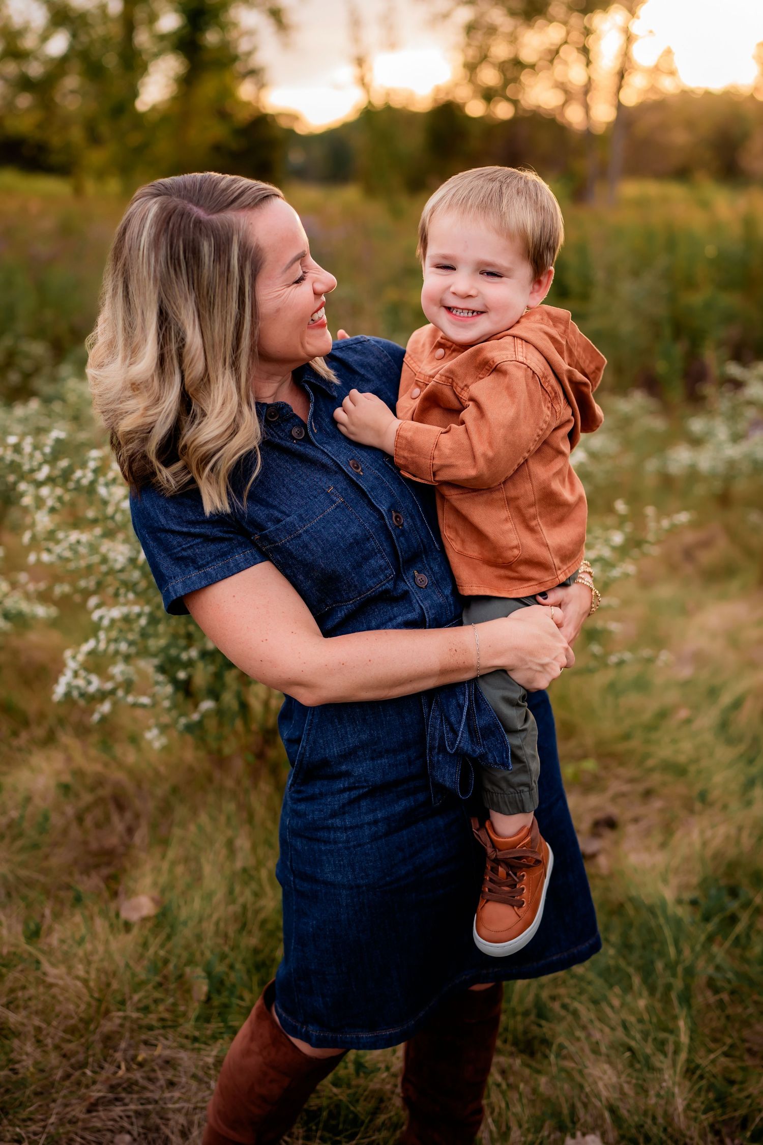 Mother and child share joyful moment in golden sunset field with wildflowers.
