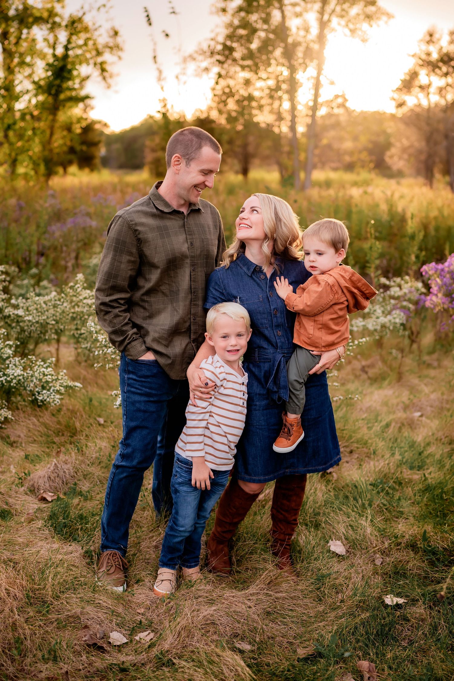 Family of four poses together in wildflower field during sunset.