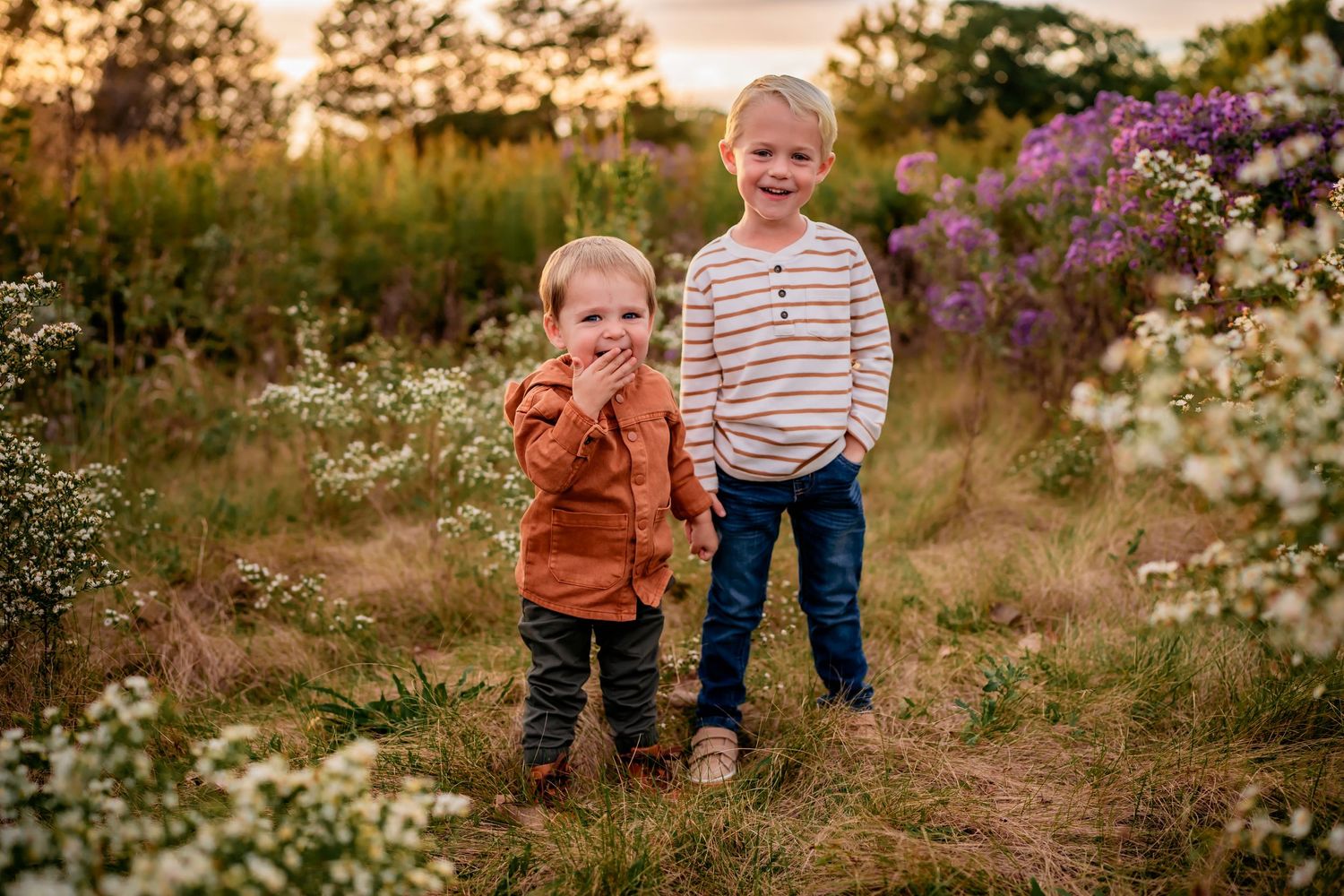 Two children standing together in blooming wildflower meadow at sunset.