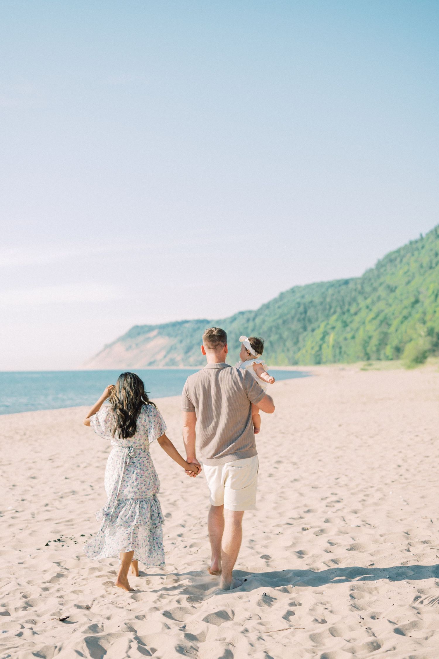 Family walking together on sandy beach with mountains in background.