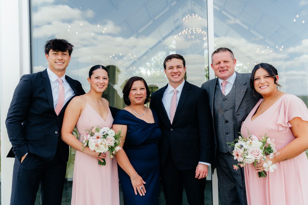 Wedding party members pose together in front of a clear tent on a sunny day with blue skies.