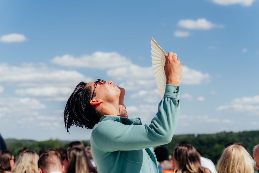 Woman in mint green sweater joyfully holds up and gazes at a white paper butterfly against a blue summer sky.