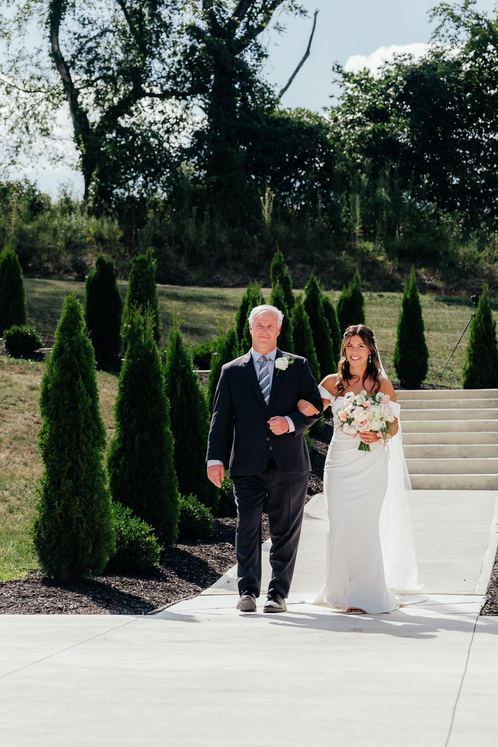 A wedding ceremony at an outdoor venue with stone stairs and elegant cypress trees lining the path.