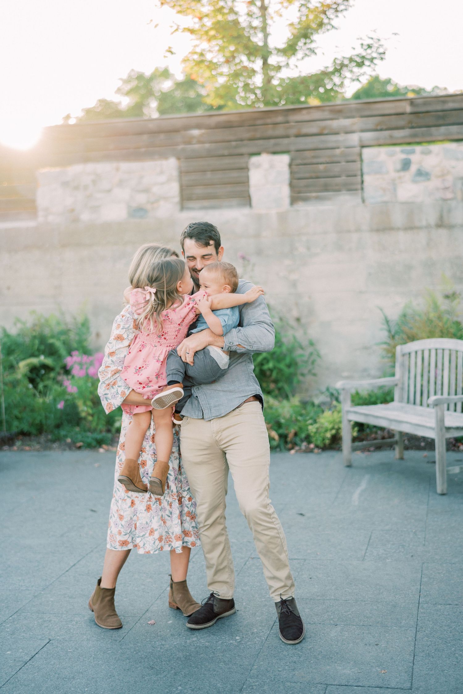 A family shares a tender moment together on a garden patio during golden hour with sunlight glowing behind them.