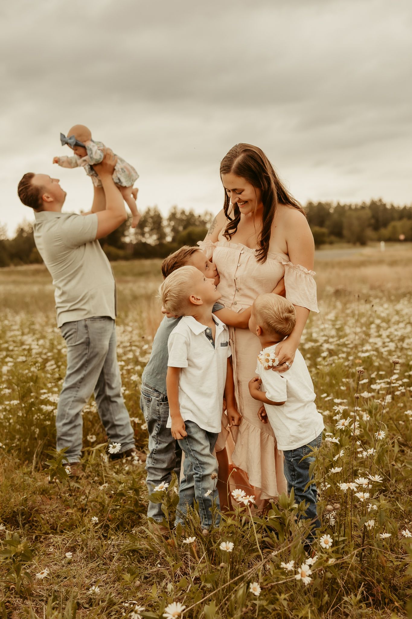 A couple shares an intimate moment in a golden field at sunset while holding a smiling baby.