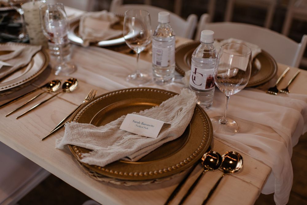 Elegant place setting at wedding reception with gold charger plate, white linens, and crystal glassware on table.