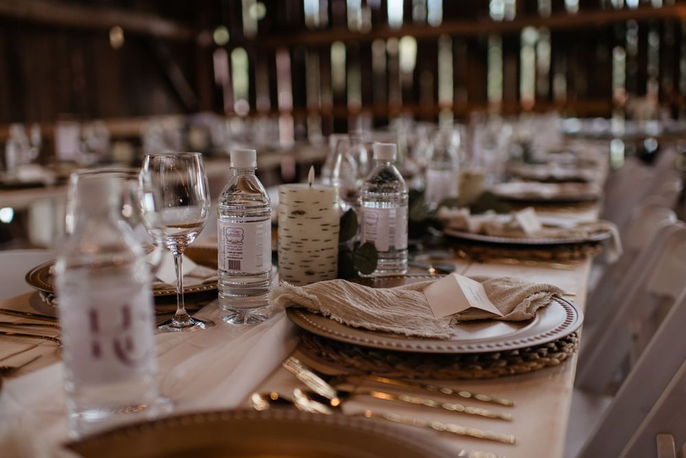 Rustic wedding table setting with charger plates, wine glasses, and personalized bottle favors in warm lighting.