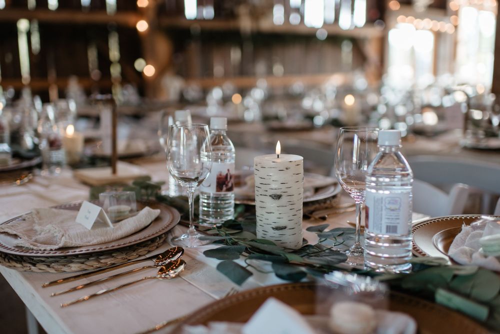 Close-up of an elegant table setting with birch candles, greenery runners, and wine glasses in a rustic venue.