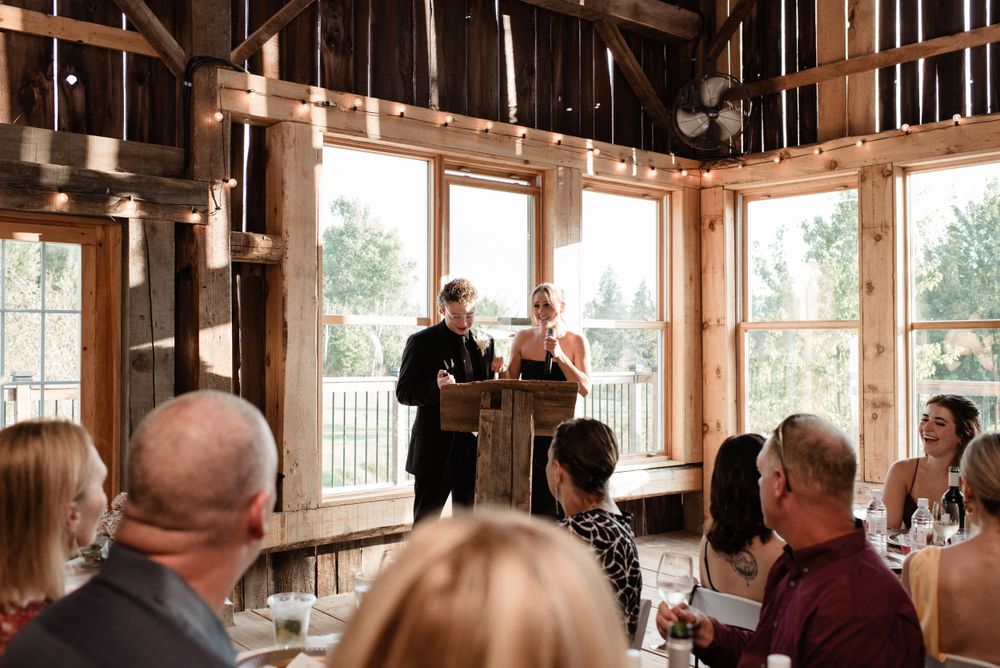 An intimate wedding ceremony takes place inside a rustic wooden venue with large windows and natural light streaming in.