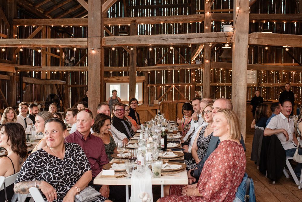 Wedding guests enjoying dinner at communal tables inside a warmly lit historic barn venue.