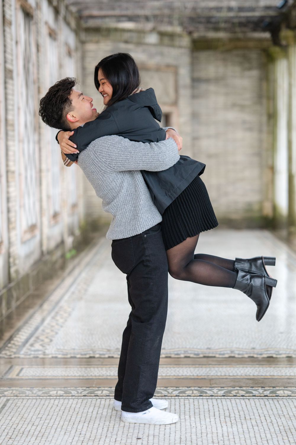 A joyful couple celebrating with a playful lift in an architectural setting after getting engaged