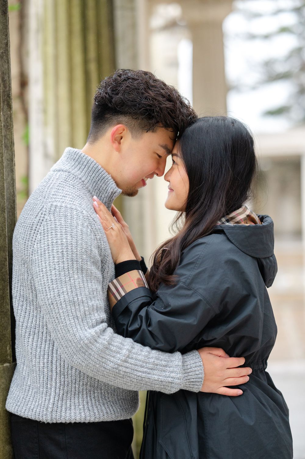 Young couple shares an intimate romantic moment outdoors on a rainy day after a proposal in Untermyer Gardens